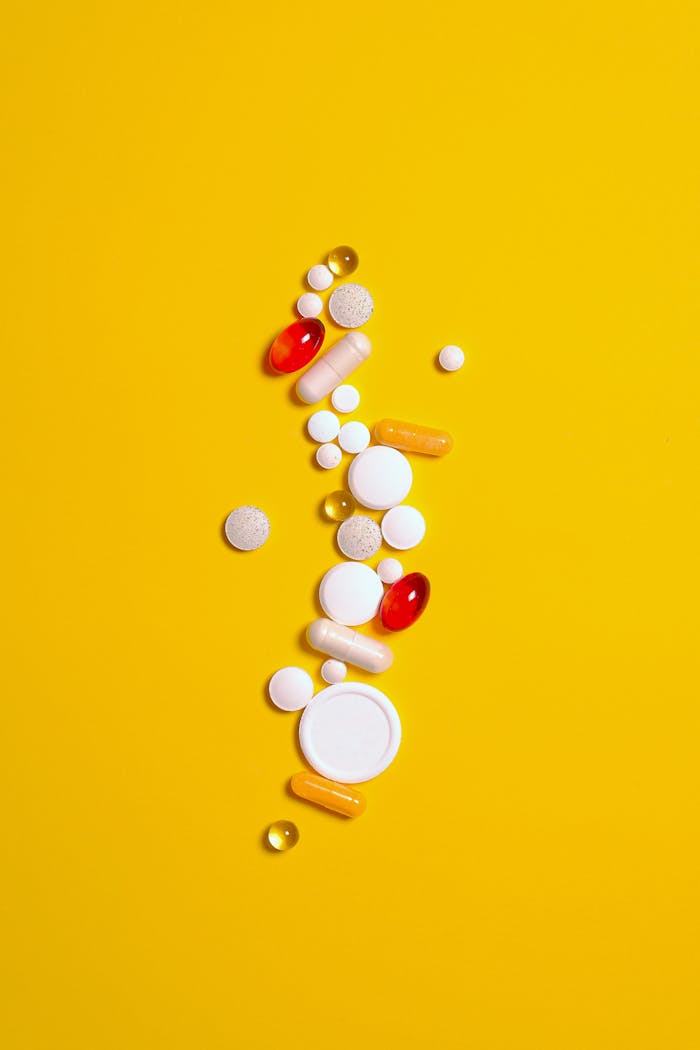 Assorted pills in vibrant colors on a striking yellow background, representing healthcare and medicine.