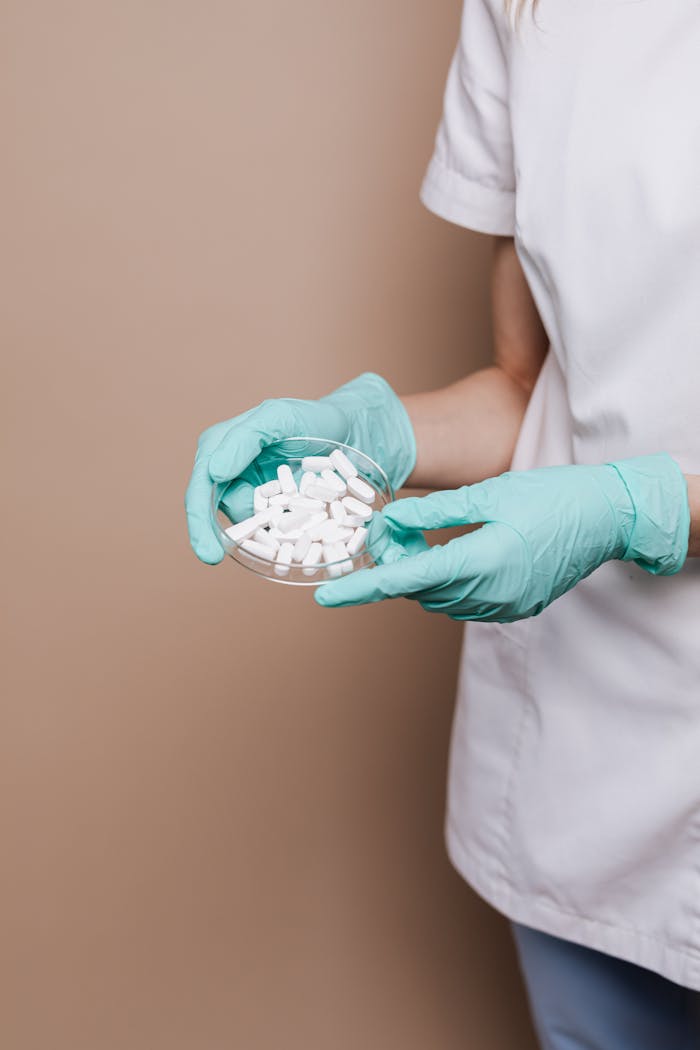 Medical professional holding white pills in a petri dish wearing teal gloves, highlighting healthcare and sterile conditions.
